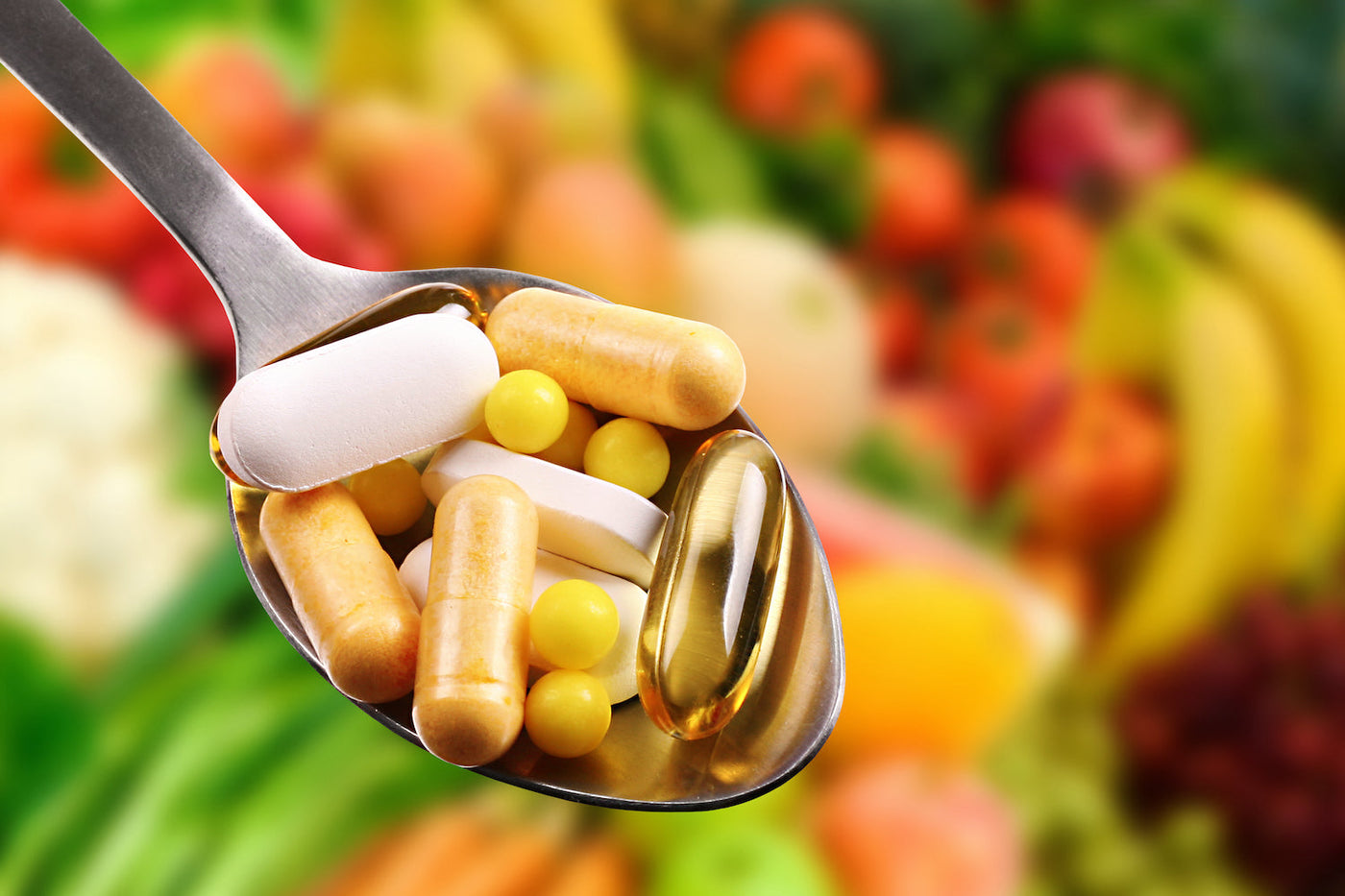 Variety of Vitamins held in a spoon against a background of healthy fruit and vegetables