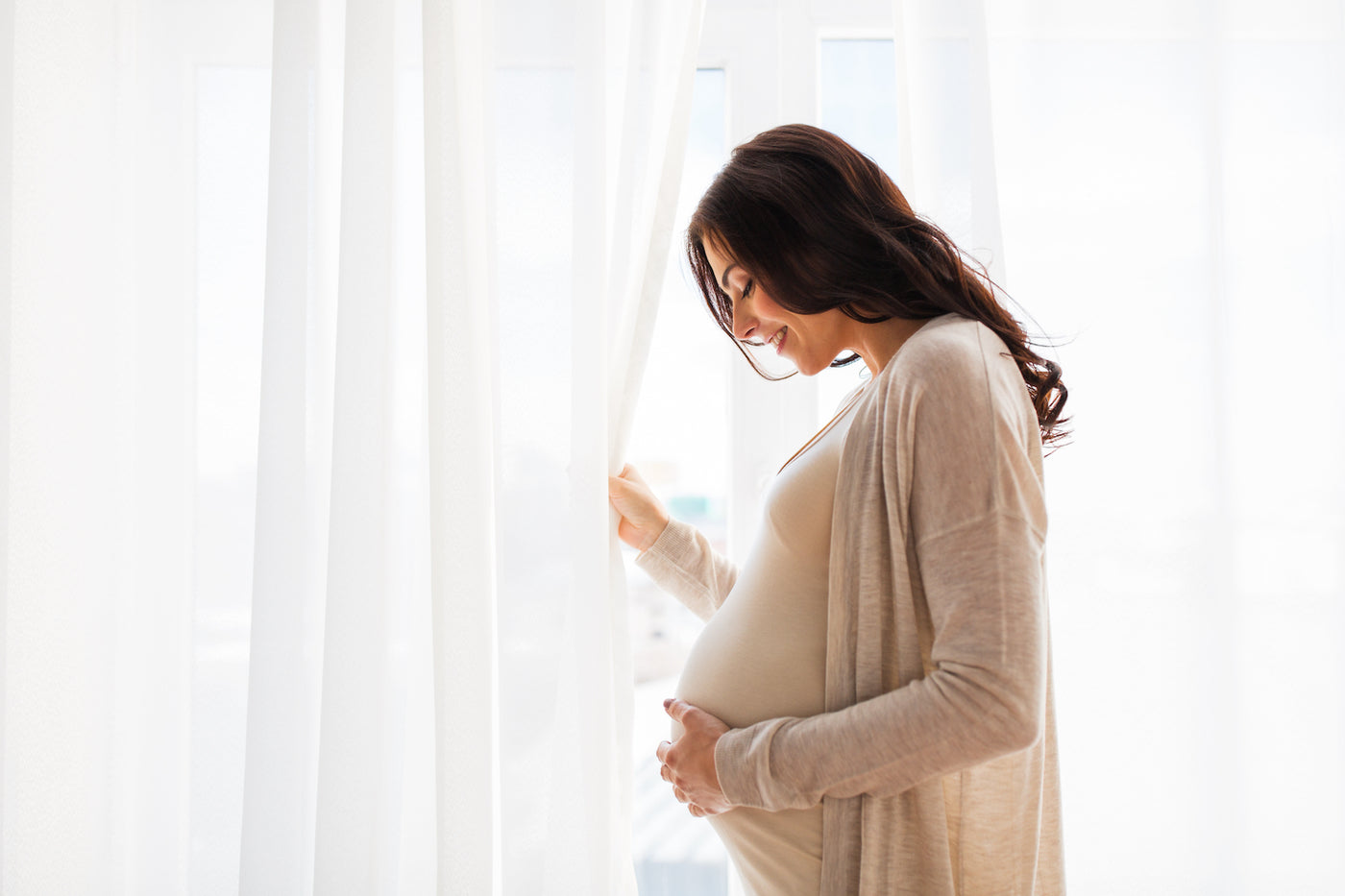 Young, heavily pregnant woman holding her bump by a large airy window