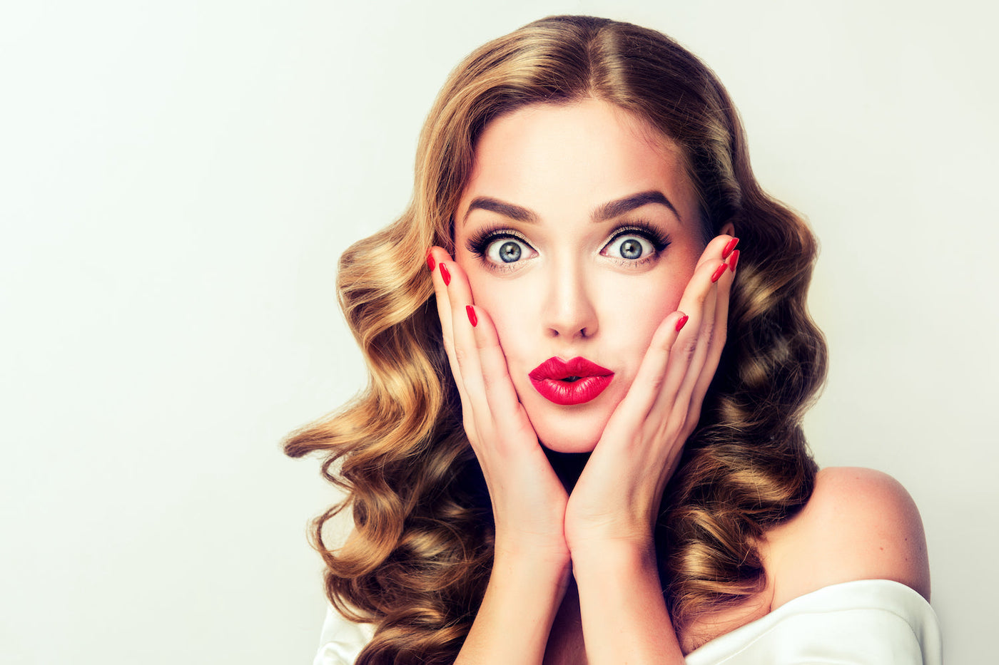 Beautiful young woman with sixties makeup and hair holding her face in surprise with both hands
